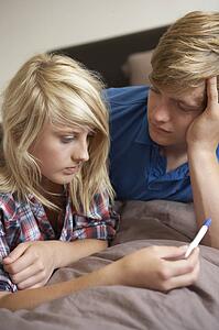 Two Teenage Girls Lying On Bed Looking At Pregnancy Testing Kit