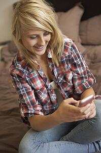 Teenage Girl Lying In Bedroom Using Mobile Phone