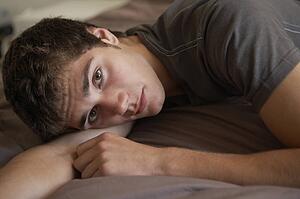 Depressed Teenage Boy Lying In Bedroom