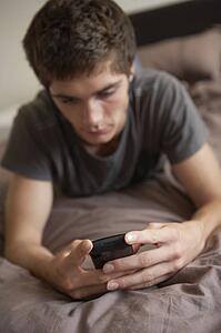 Unhappy Teenage Boy Lying In Bedroom With Mobile Phone