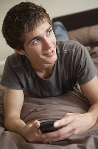 Teenage Boy Lying In Bedroom Using Mobile Phone