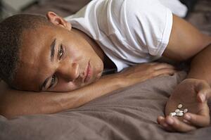 Depressed Teenage Boy Lying In Bedroom With Pills