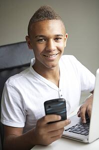 Teenage Boy Using Laptop And Mobile At Home