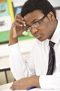 Stressed Male Teenage Student Studying In Classroom
