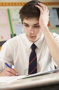 Stressed Male Teenage Student Studying In Classroom