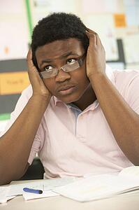 Stressed Male Teenage Student Studying In Classroom