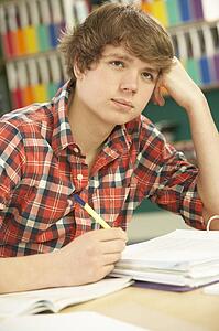 Stressed Male Teenage Student Studying In Classroom