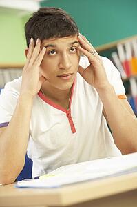 Stressed Male Teenage Student Studying In Classroom