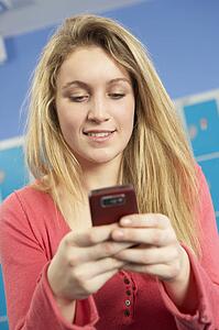 Female Teenage Student Using Mobile Phone By Lockers In School