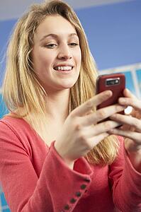 Female Teenage Student Using Mobile Phone By Lockers In School