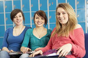 Female Teenage Students Relaxing By Lockers In School