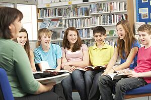 Teenage Students In Library Reading Books With Tutor