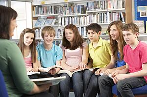 Teenage Students In Library Reading Books With Tutor