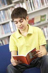 Male Teenage Student In Library Reading Book