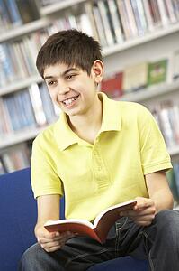 Male Teenage Student In Library Reading Book