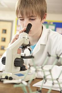 Male Teenage Student In Science Class Looking Through Microscope