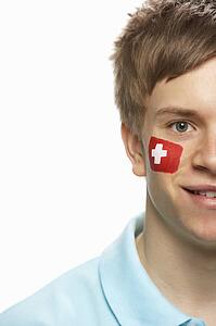 Young Male Sports Fan With Swiss Flag Painted On Face