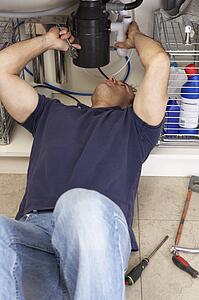 Plumber Working On Sink In Kitchen