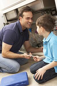 Son Helping Father To Mend Sink In Kitchen