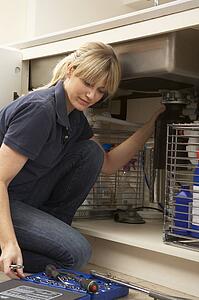 Female Plumber Working On Sink In Kitchen
