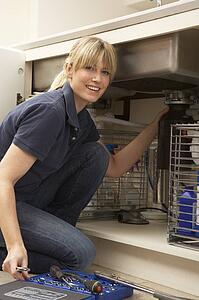 Female Plumber Working On Sink In Kitchen