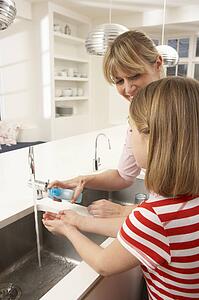 Mother And Daughter Washing Hands At Kitchen Sink