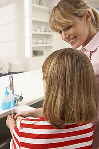 Mother And Daughter Washing Hands At Kitchen Sink