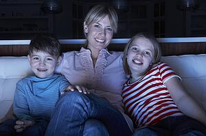 Mother And Children Watching Programme On TV Sitting On Sofa Together