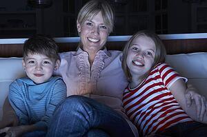 Mother And Children Watching Programme On TV Sitting On Sofa Together