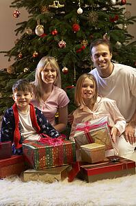 Family Opening Christmas Present In Front Of Tree