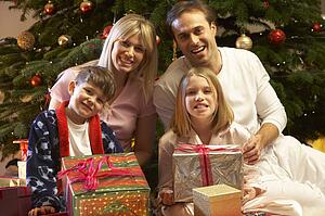 Family Opening Christmas Present In Front Of Tree