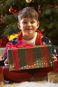 Young Boy Opening Christmas Present In Front Of Tree