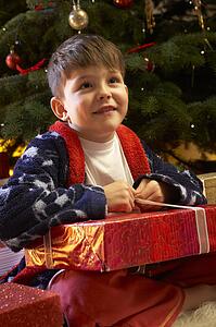 Young Boy Opening Christmas Present In Front Of Tree