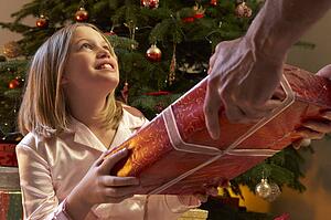 Young Girl Receiving Christmas Present In Front Of Tree