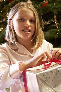 Young Girl Opening Christmas Present In Front Of Tree