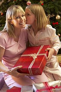 Daughter Giving Mother Christmas Present In Front Of Tree