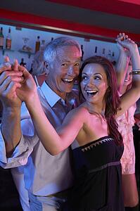 Senior Man Dancing With Younger Woman In Busy Bar
