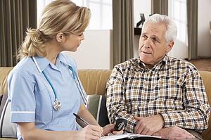 Senior Man Talking To Health Visitor At Home
