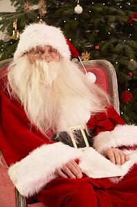 Santa Claus Sitting In Armchair In Front Of Christmas Tree