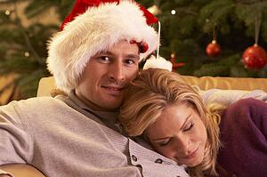 Tired Couple Relaxing In Front Of Christmas Tree
