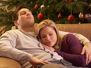Tired Couple Relaxing In Front Of Christmas Tree