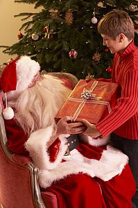 Santa Claus Giving Gift To Boy In Front Of Christmas Tree