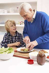 Grandfather And Grandson Making Sandwich In Kitchen