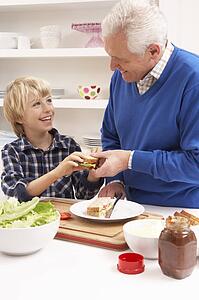 Grandfather And Grandson Making Sandwich In Kitchen