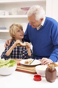 Grandfather And Grandson Making Sandwich In Kitchen