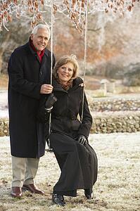 Senior Couple Sitting On Garden Swing In Frosty Landscape