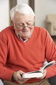 Senior Man Relaxing In Chair At Home Reading Book
