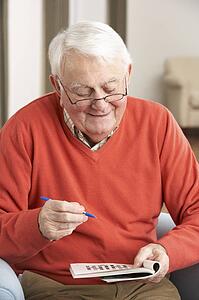 Senior Man Relaxing In Chair At Home Completing Crossword