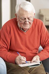 Senior Man Relaxing In Chair At Home Completing Crossword