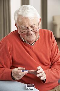Senior Man Checking Blood Sugar Level At Home